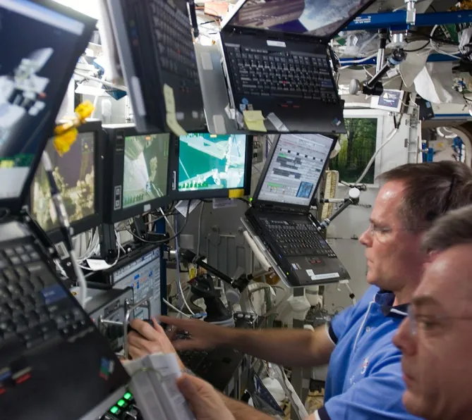 Photo de deux hommes s’affairant devant les écrans du poste de travail du téléopérateur de Canadarm2.