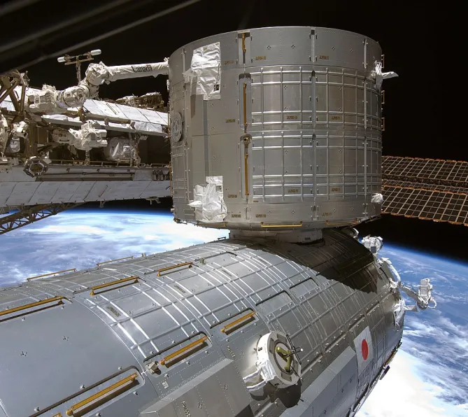 Photo du laboratoire japonais Jem attaché à la Station spatiale internationale, vu de l’extérieur dans l’espace. Il s’agit d’une grosse structure cylindrique métallique.